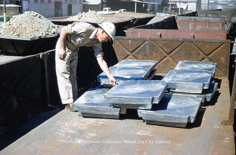 Worker inspecting cast lead blocks on train at Lead Smelter, Mount Isa Mines, c.1956