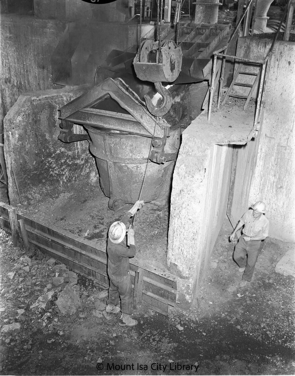 Crane chaser connecting crane hook to pot bridle at Copper Smelter, Mount Isa Mines, c.1956