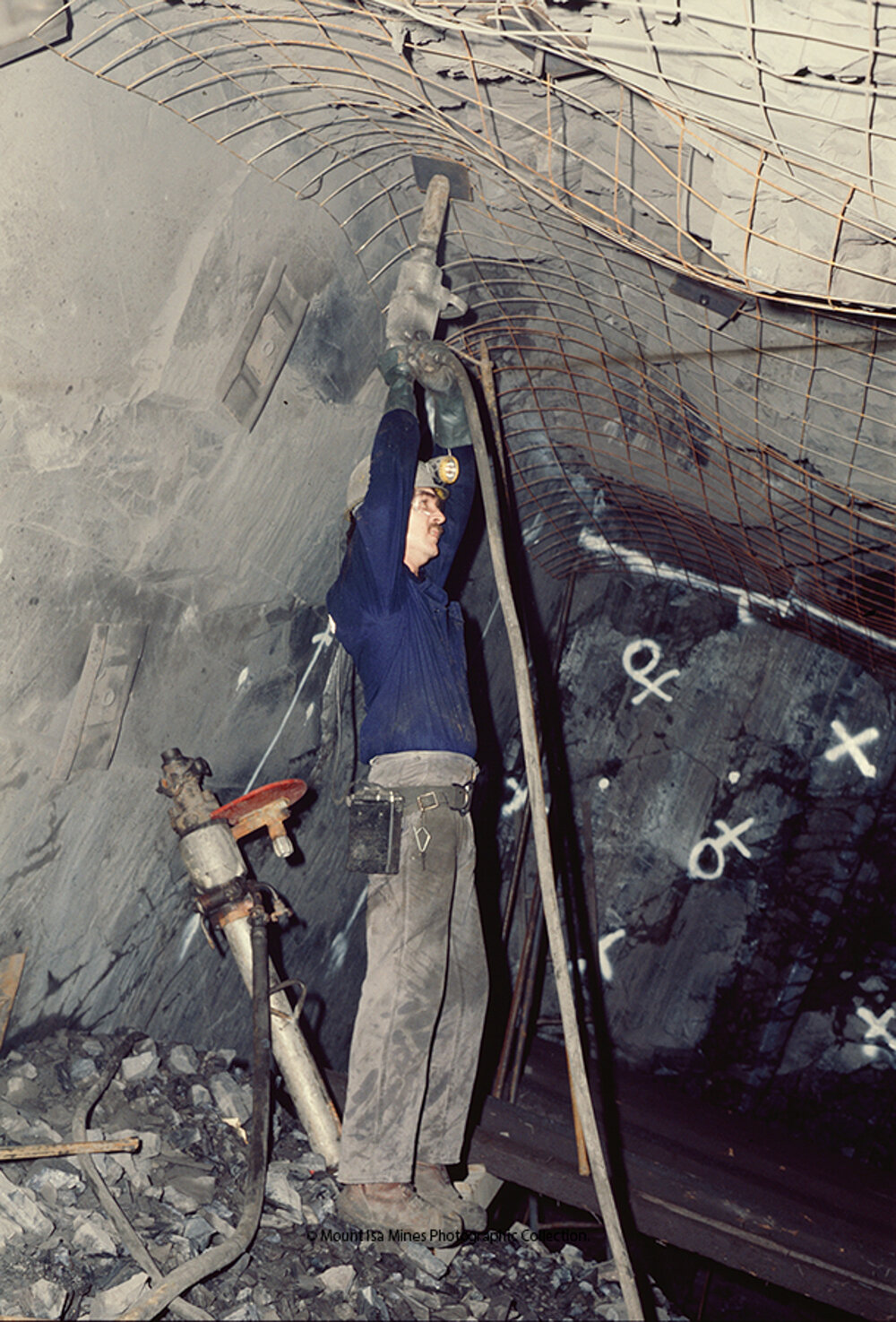 Underground worker bolting mesh plate to ground support in lead mine, Mount Isa Mines, c.1986
