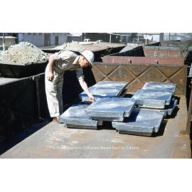 Worker inspecting cast lead blocks on train at Lead Smelter, Mount Isa Mines, c.1956